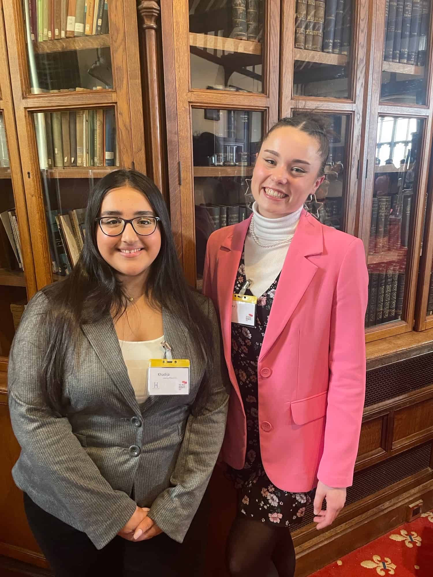 Cheadle Hulme Sixth Form student Lucy stands next to Laurus Ryecroft student Khadija in front of a bookshelf