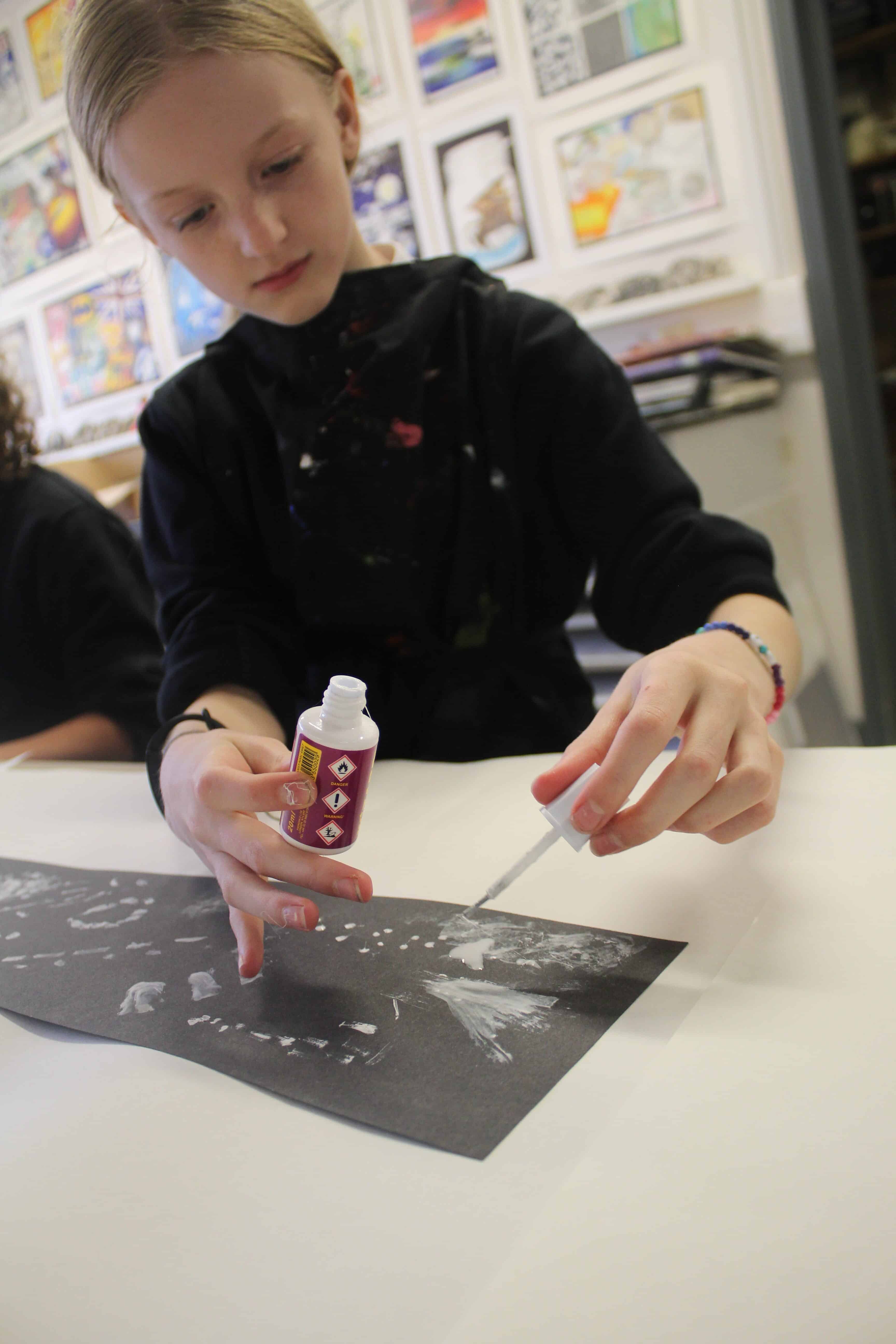 A student paints with white Tippex on black paper to create mark making of insect sounds during a sound painting workshop for the Big Draw 2023.