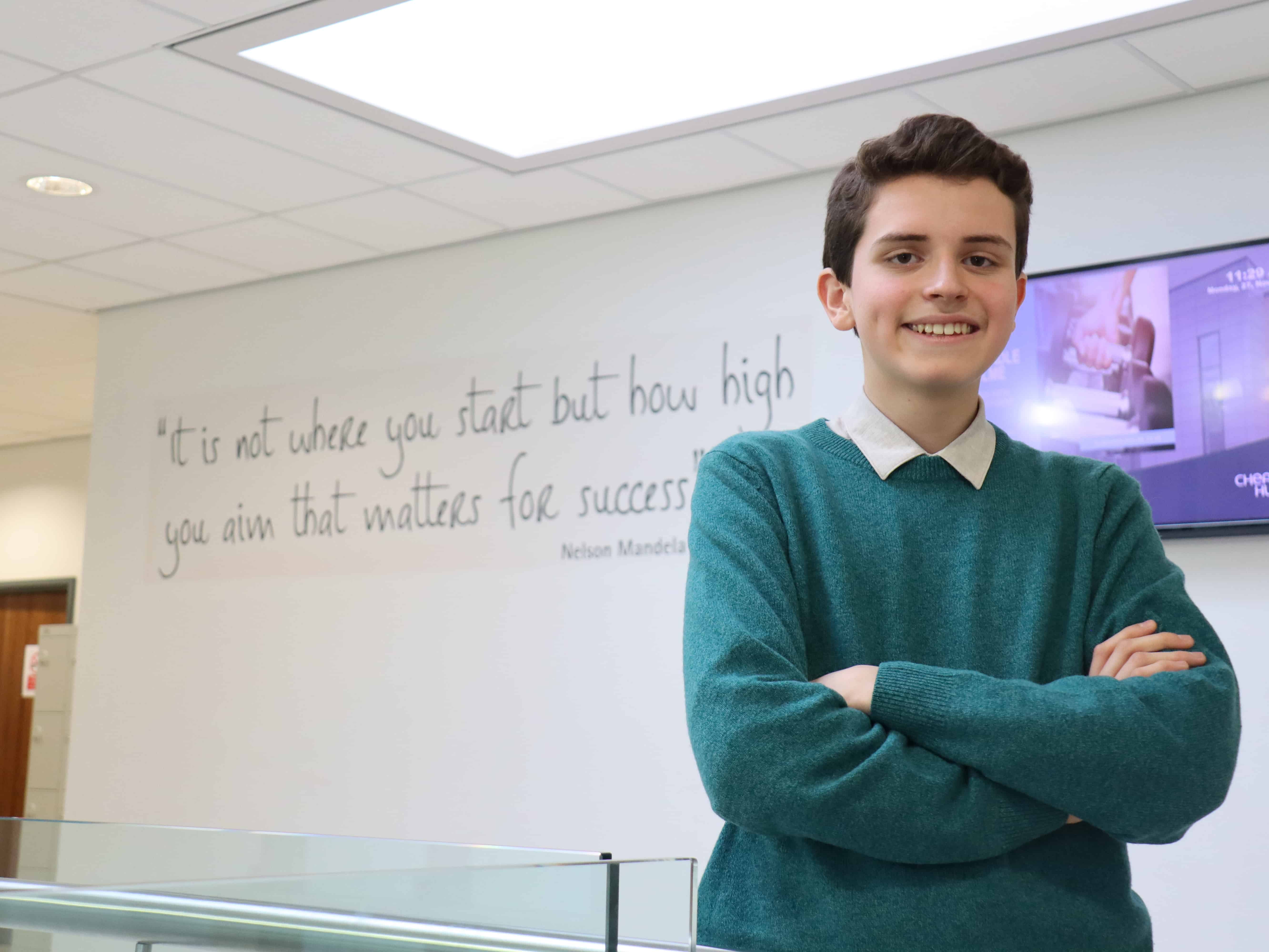 Cheadle Hulme Sixth Form student and Member of UK Youth Parliament, Rodrigo Palmer stands in the Sixth Form building in front of a wall that reads: "It is not where you start but how high you aim that matters for success"