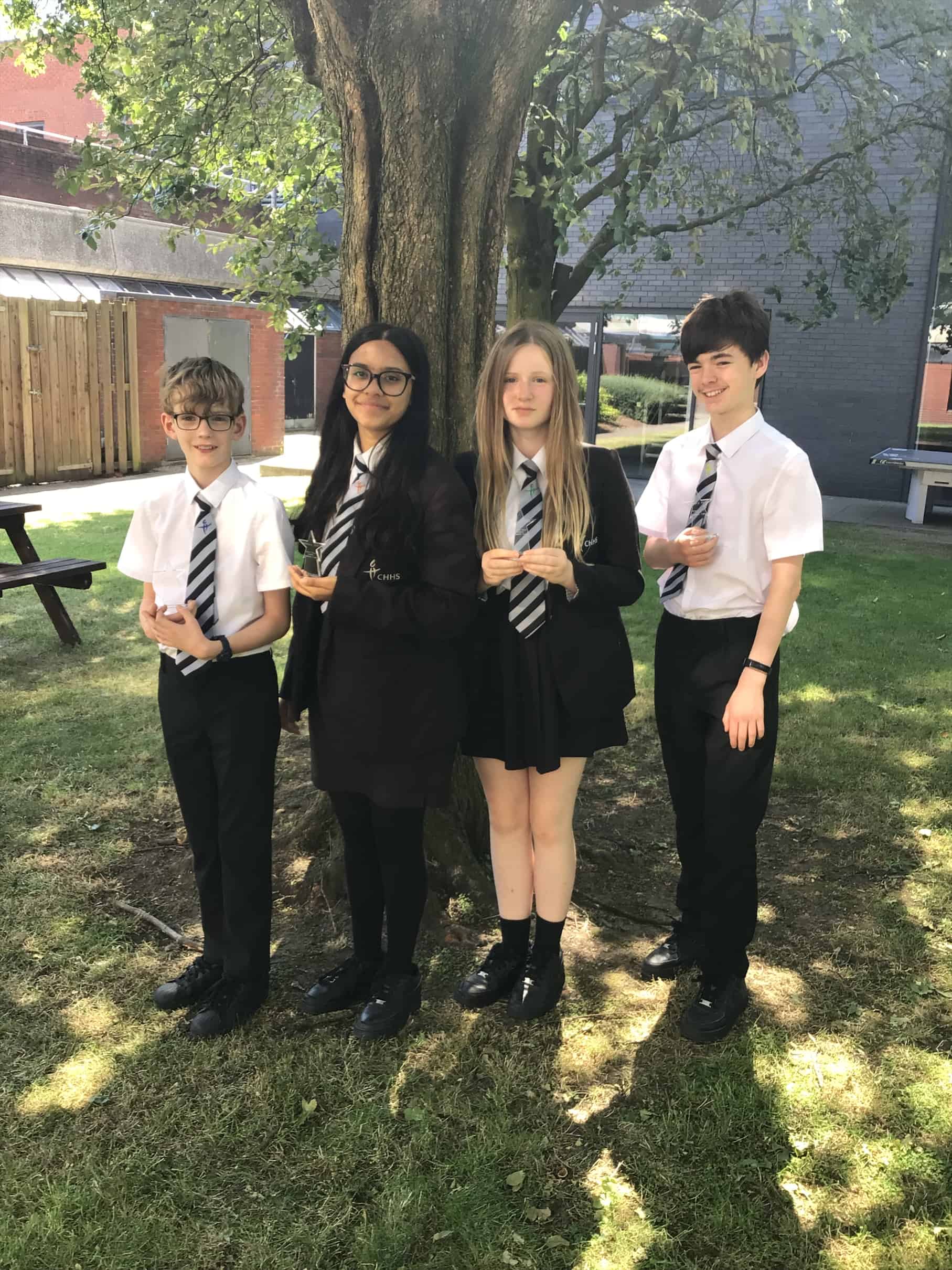 Four Cheadle Hulme High School students stand outside smiling and holding their Kathryn Oliver Leonard Teamwork trophies, earned from the Chemquiz