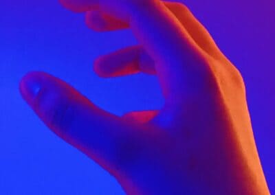 A close-up shot of a hand in a space lit with blue and red lights. The light of the red hits the knuckles creating a stark contrast of colours.