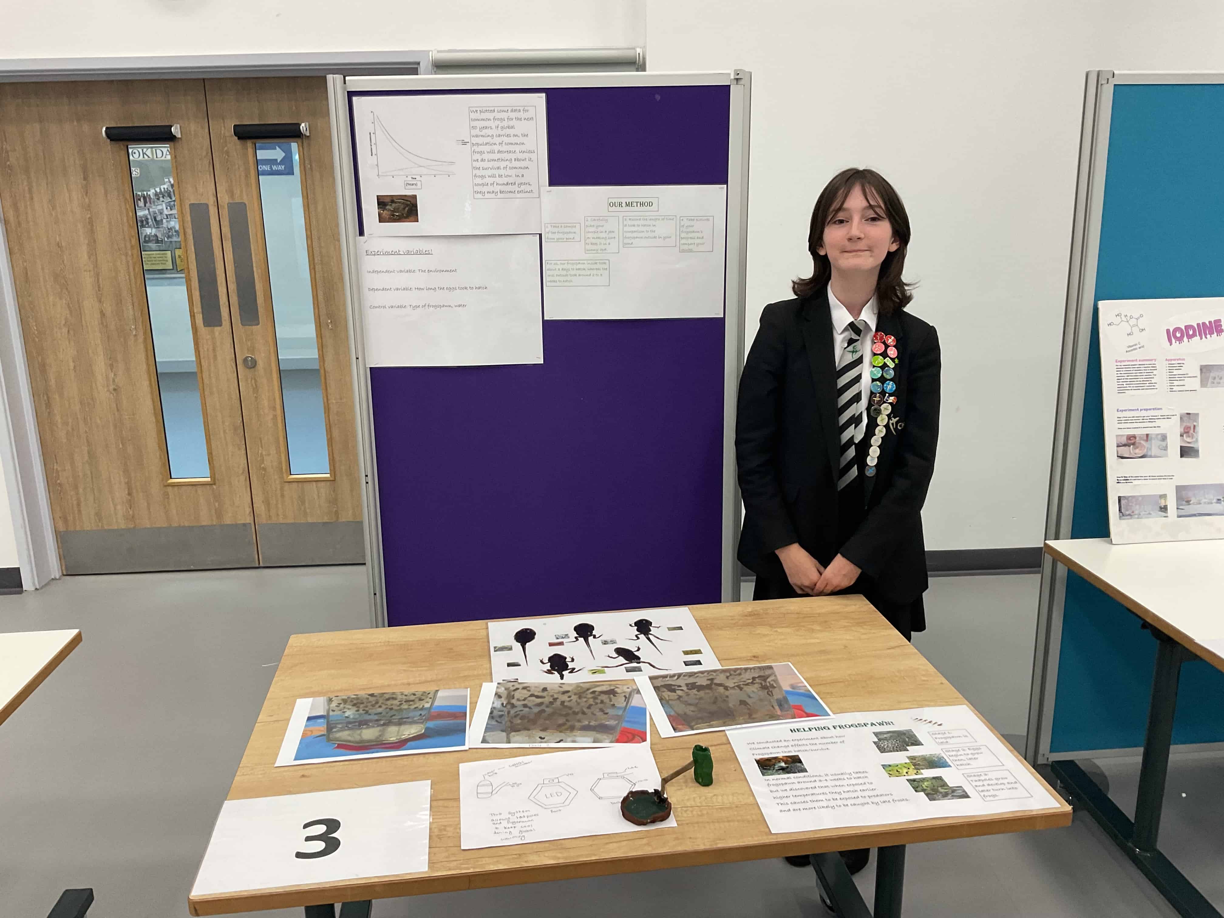 A Cheadle Hulme High School student from Team Frogspawn represents the team of 4 at the Laurus Trust Science Fair as she smiles in front of their project at Laurus Cheadle Hulme.