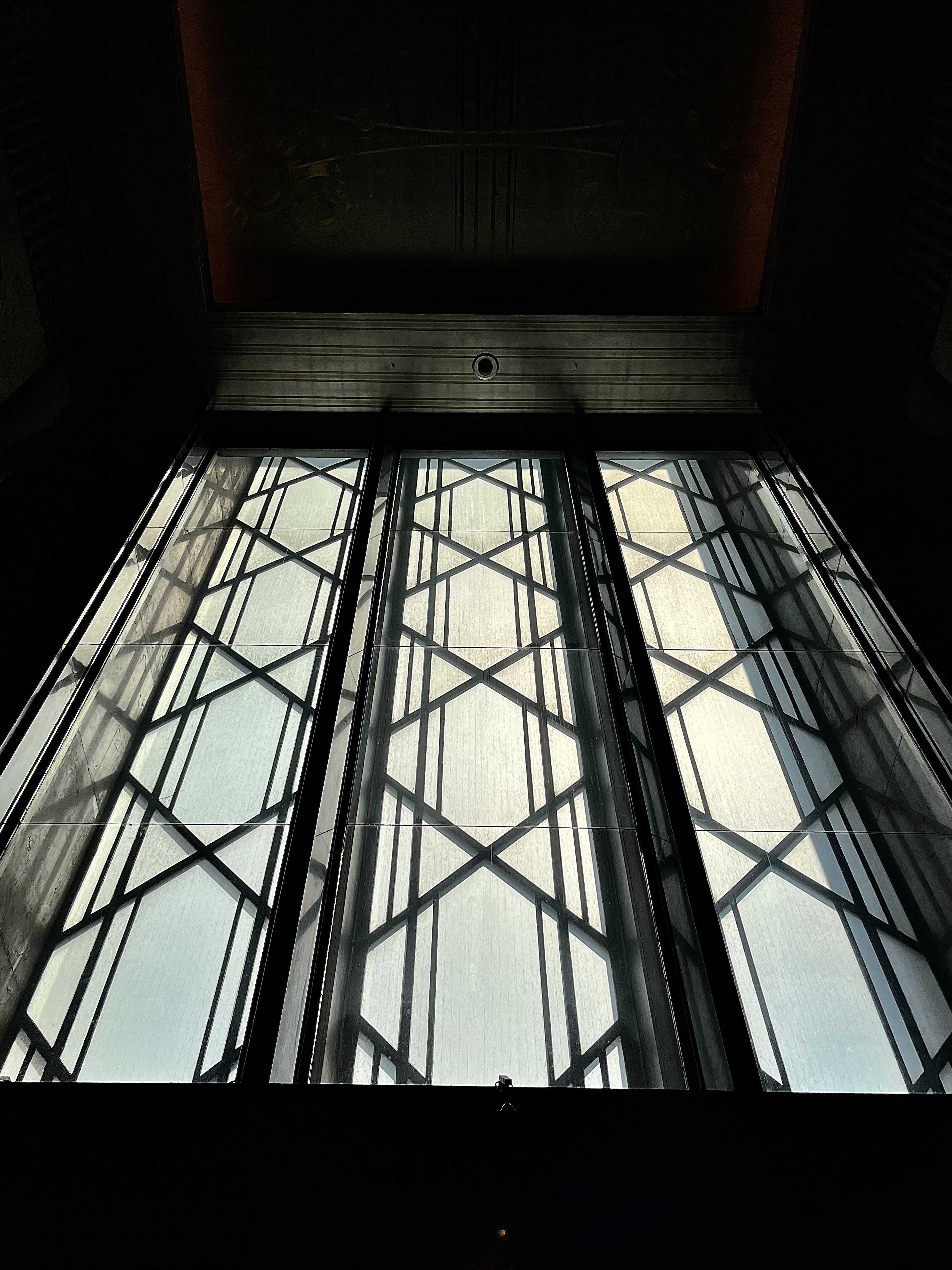 A low angle darkly lit shot looking up at a window with unique lines and patterns on its panes, by Grace in Year 10, runner up in Cheadle Hulme High School Photography Calendar Competition 2024.